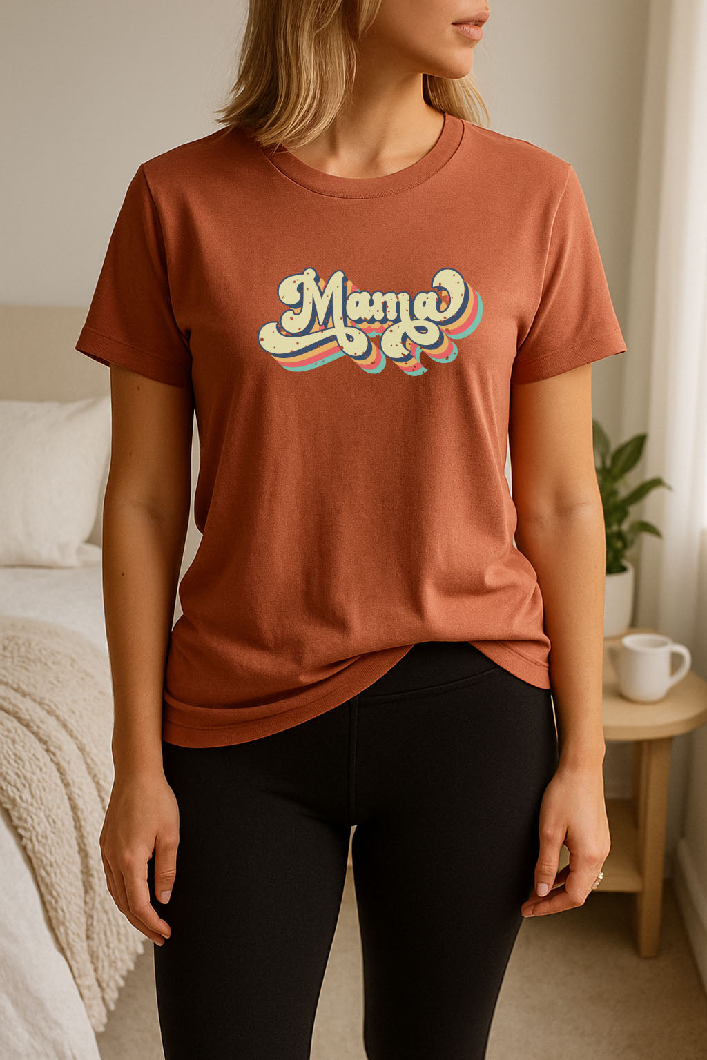 Person wearing a rust t-shirt with 'Mama' printed on it in a bedroom setting.