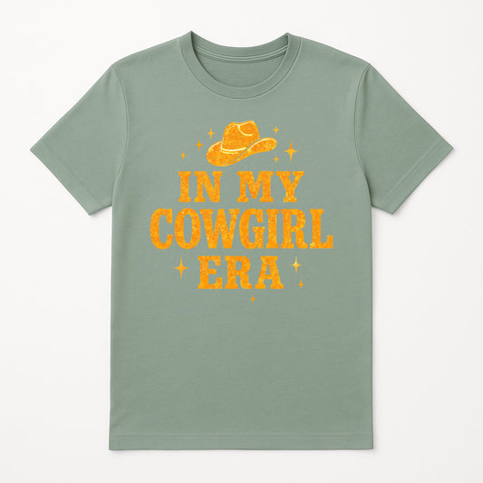 In My Cowgirl Era graphic t-shirt in sage green, Western country music inspired tee with bold distressed lettering and cowboy hat design, trendy cowgirl aesthetic shirt for women