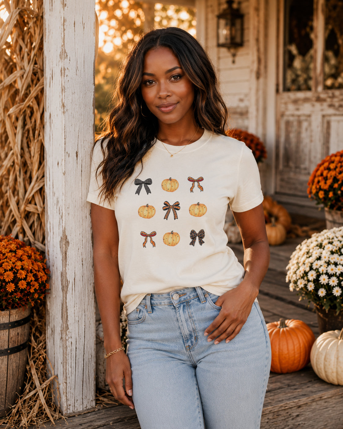 Woman wearing the Bows & Boos pumpkin bow graphic tee on a cozy autumn porch surrounded by pumpkins, mums, and fall décor.