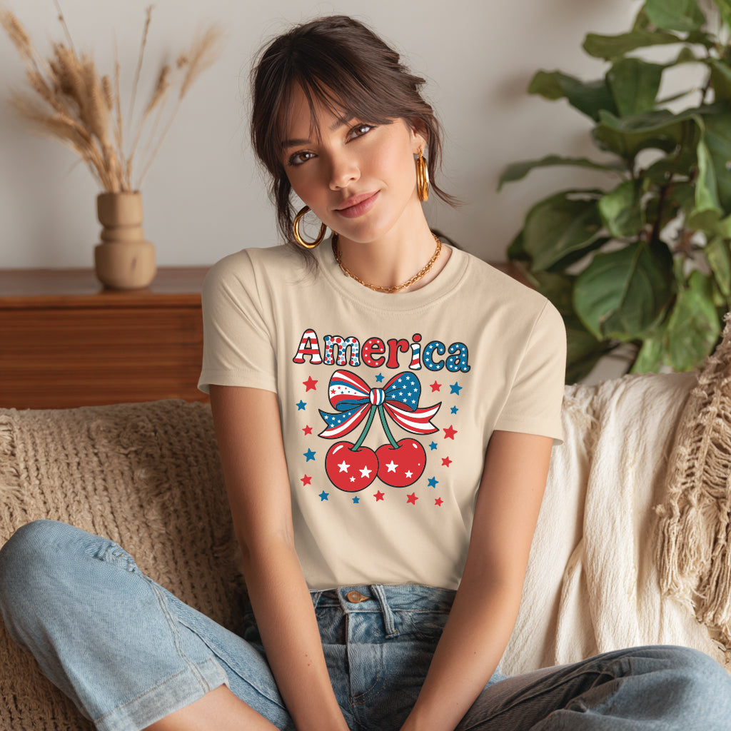 Model wearing beige America cherry coquette patriotic graphic t-shirt with bow and stars