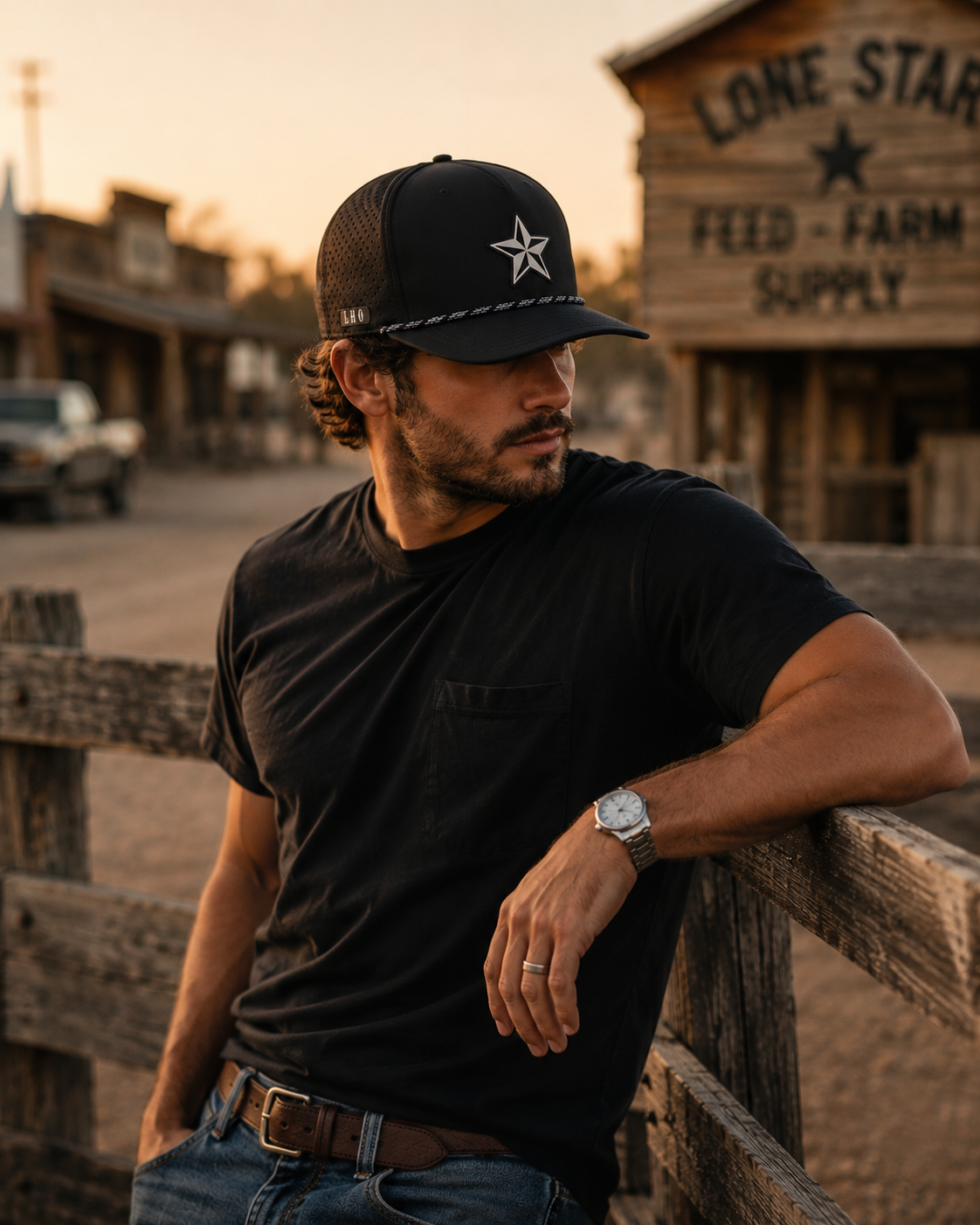 Man wearing a black Texas star performance rope hat with perforated side panels, standing against a rustic ranch fence at golden hour. Western lifestyle photography by Lonestar Heritage Outpost.