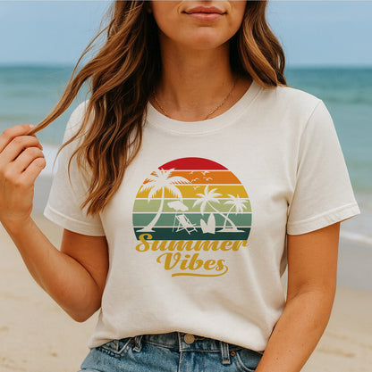 Women's Summer Vibes graphic tee with retro sunset and palm trees design, worn seated on the beach.